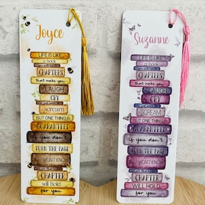 May include: Two decorative bookmarks with tassels. One bookmark has the name "Joyce" and a gold tassel, the other has the name "Suzanne" and a pink tassel. Both bookmarks feature a stack of books with inspirational text.