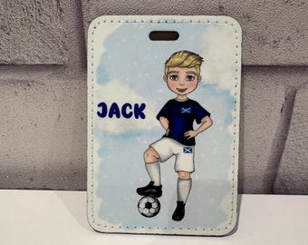 Pode incluir: Uma etiqueta de bagagem retangular com uma ilustração de desenho animado de uma criança loira com uma camisola de futebol azul-escura e calções brancos, de pé com um pé sobre uma bola. O nome JACK está impresso a azul num céu azul-claro.