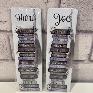 May include: Two white bookmarks with gray tassels. Each bookmark features a stack of books with the words "LIFE IS LIKE" and other phrases. One bookmark says "Harry" and the other says "Joe".