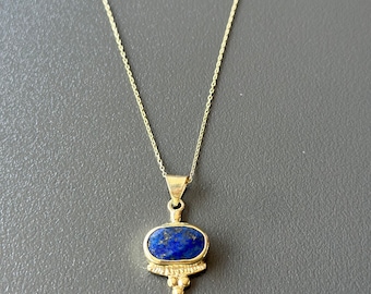 May include: A gold chain necklace with a pendant featuring a blue oval lapis lazuli stone set in a gold bezel. The pendant has a decorative design with three small gold balls.