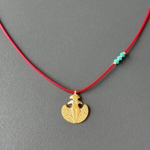 May include: A gold pendant necklace with a stylized female figure design. The necklace is on a red cord with turquoise beads.