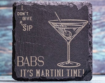 May include: Square black slate coaster with etched martini glass design and the phrase "I don't give a sip, Babs, it's martini time!". The coaster has a rough, natural edge and is suitable for barware.