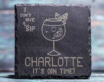 May include: A square, dark gray slate coaster with etched text and a cocktail glass design. The text reads "I DON'T GIVE A SIP" and "CHARLOTTE IT'S GIN TIME!". The cocktail glass has a lemon slice and garnish.