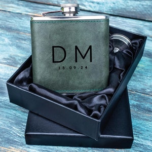 Könnte beinhalten: Eine grüne, lederbezogene Trinkflasche mit silbernem Deckel und einer schwarzen Box. Die Flasche trägt die Initialen "DM" und das Datum "15.09.24" eingraviert.