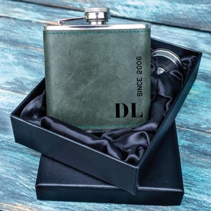 Op de afbeelding: Een groene leren fles met een zilveren deksel en een zwarte doos. De fles is gegraveerd met de initialen "DL" en de tekst "Since 2006".