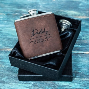 Peut inclure: Une flasque en cuir marron avec un couvercle argenté et une inscription noire qui dit "Daddy Love Evie, Betsy & Amelia X". La flasque est dans un coffret cadeau noir avec une doublure en satin noir.