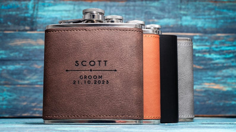 May include: A collection of personalized flasks in brown, orange, black, and gray leather. The front flask is engraved with "SCOTT", "GROOM", and the date "21.10.2023". Each flask has a silver cap.