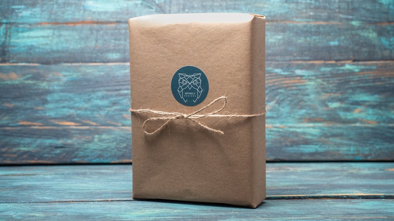 May include: A rectangular package wrapped in brown paper, tied with twine, and sealed with a round sticker. The sticker features a geometric owl design and the text "WONBLY DESIGNS". The package is set against a blue and teal wooden background.