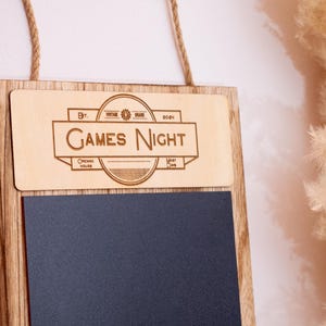 May include: A wooden sign with a chalkboard insert. The top of the sign has a laser-engraved design that says "Games Night".