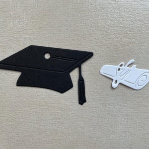 Peut inclure: Une découpe de chapeau de graduation noir et de diplôme blanc. Le chapeau a un gland et le diplôme est roulé.