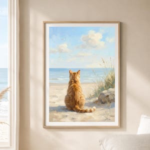 May include: A framed print depicts an orange tabby cat sitting on a sandy beach, gazing out at the ocean. The artwork features a blue sky with fluffy white clouds, gentle waves, and tall beach grass. The cat's back is turned to the viewer.