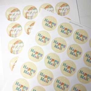 May include: Sheets of round stickers with the words "Happy Mail" in various colors, including purple, orange, and teal. Each sticker has a light yellow background and a watercolor rainbow design. The stickers are for packaging and crafts.