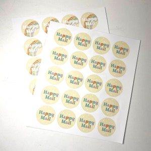 May include: Sheets of round stickers with the words "Happy Mail" in colorful letters. Each sticker has a light yellow background with a rainbow and star design. The stickers are on a white background.
