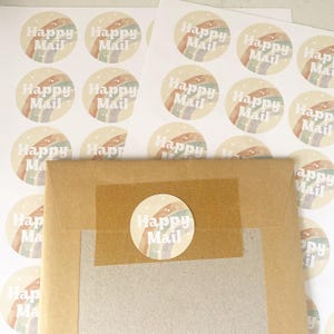 May include: Round stickers with a rainbow design and the words "Happy Mail" in a soft, off-white font. The stickers are scattered around a brown paper envelope sealed with a matching sticker.