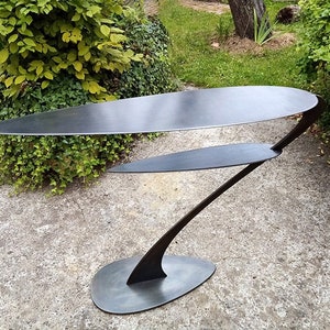 Peut inclure: Une table moderne en métal noir avec deux étagères et un design unique et abstrait. La table a un look élégant et minimaliste et serait un ajout élégant à n'importe quelle maison.
