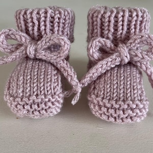 Puede incluir: Un par de patucos de beb&eacute; de punto en color malva suave. Cada patuco presenta un lazo decorativo hecho con el mismo hilo. Los patucos tienen un pu&ntilde;o acanalado y un patr&oacute;n de punto texturizado.