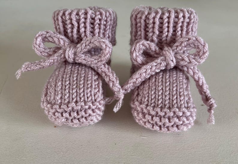 Puede incluir: Un par de patucos de beb&eacute; de punto en color malva suave. Cada patuco presenta un lazo decorativo hecho con el mismo hilo. Los patucos tienen un pu&ntilde;o acanalado y un patr&oacute;n de punto texturizado.