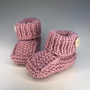 Peut inclure: Une paire de chaussons pour bébé en tricot rose avec un bouton sur un chausson.