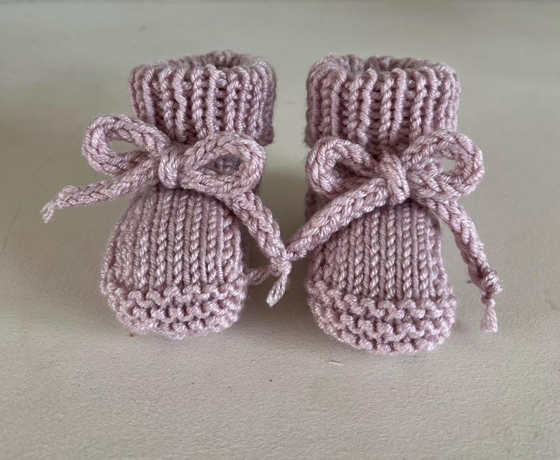 Puede incluir: Un par de patucos de beb&eacute; tejidos en color lavanda suave. Cada patuco tiene un lazo decorativo en la parte delantera. Los patucos est&aacute;n hechos de hilo texturizado, un regalo encantador para un reci&eacute;n nacido.