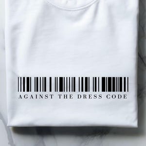 May include: A folded white t-shirt with a black barcode design and the text "AGAINST THE DRESS CODE" printed below. The shirt is made of a soft material and is displayed on a marble surface.