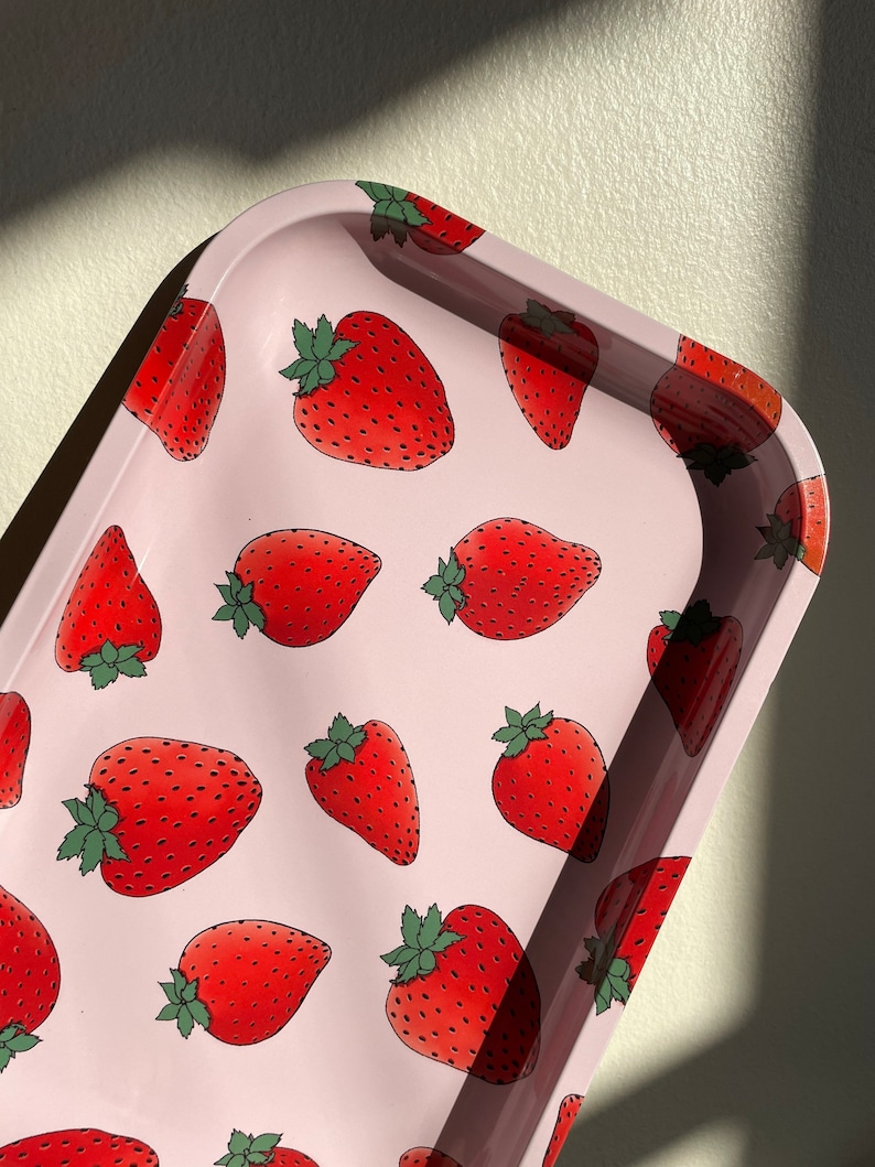 Puede incluir: Una bandeja de metal rosa con un patr&oacute;n repetido de fresas rojas. Las fresas tienen hojas verdes y est&aacute;n delineadas en negro.