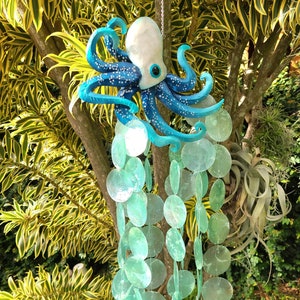 May include: A blue and white octopus wind chime with a string of light green, iridescent, round, shell-like ornaments hanging from it.