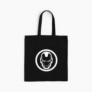 May include: Black tote bag featuring a white Iron Man helmet logo inside a white circle. The bag has black handles and is made of a durable fabric. The design is simple and bold, perfect for carrying books or groceries.