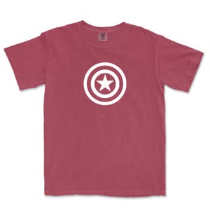 Puede incluir: Camiseta de color granate con un dise&ntilde;o gr&aacute;fico blanco de una estrella dentro de un escudo circular. La camiseta de manga corta est&aacute; hecha de un material suave y es adecuada para uso casual. El dise&ntilde;o est&aacute; centrado en la parte delantera.
