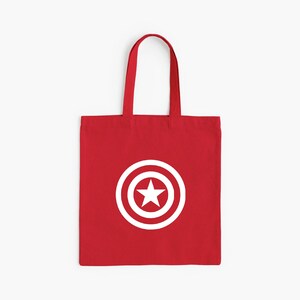 K&ouml;nnte beinhalten: Rote Tragetasche mit wei&szlig;em Captain America Schild-Design. Die Tasche hat eine rechteckige Form mit Henkel. Das Design ist ein wei&szlig;er Kreis mit einem Stern in der Mitte.