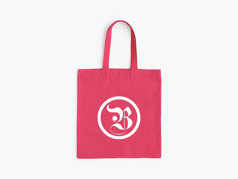 Op de afbeelding: Een felroze draagtas met een wit cirkelvormig logo met een gestileerde letter "B". De tas heeft een eenvoudig ontwerp met bijpassende roze handvatten, geschikt voor het dragen van boeken, boodschappen of persoonlijke spullen.
