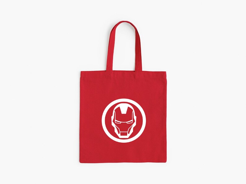 May include: Red tote bag featuring a white Iron Man helmet design inside a white circle. The bag has a rectangular shape with a handle for carrying. The design is centered on the front of the bag.