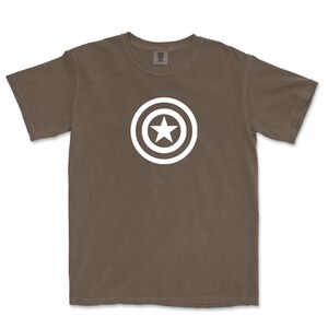 Puede incluir: Camiseta marr&oacute;n con un dise&ntilde;o gr&aacute;fico blanco de una estrella dentro de un c&iacute;rculo, que recuerda a un escudo. La camiseta es de material suave y tiene mangas cortas. El dise&ntilde;o est&aacute; centrado en el pecho.