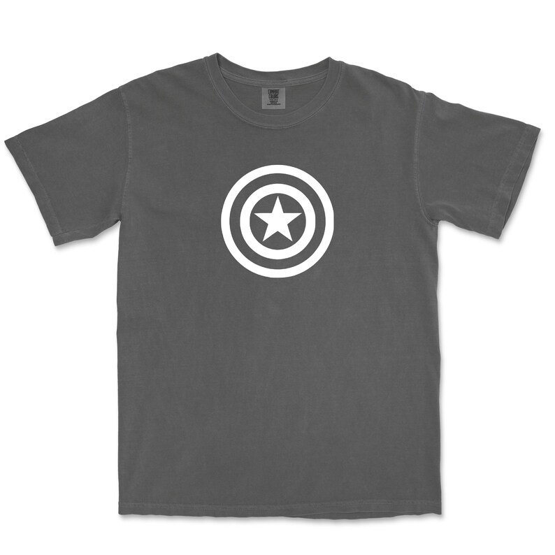 Puede incluir: Una camiseta gris oscuro con un dise&ntilde;o gr&aacute;fico blanco de una estrella dentro de un escudo circular. La camiseta tiene cuello redondo y mangas cortas. El dise&ntilde;o est&aacute; centrado en el pecho.