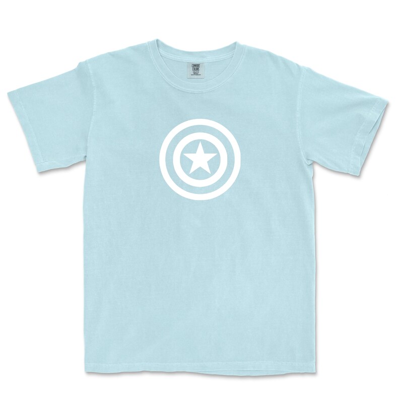 Puede incluir: Camiseta azul claro con un dise&ntilde;o gr&aacute;fico blanco de una estrella dentro de un escudo circular. La camiseta de manga corta tiene cuello redondo. El gr&aacute;fico est&aacute; centrado en la parte delantera.