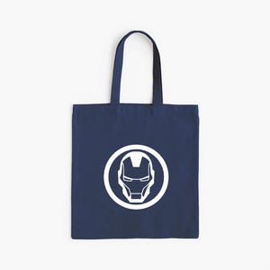 May include: Navy blue tote bag featuring a white Iron Man helmet logo inside a white circle. The bag has a rectangular shape with a handle for carrying. The design is simple and bold, suitable for everyday use.