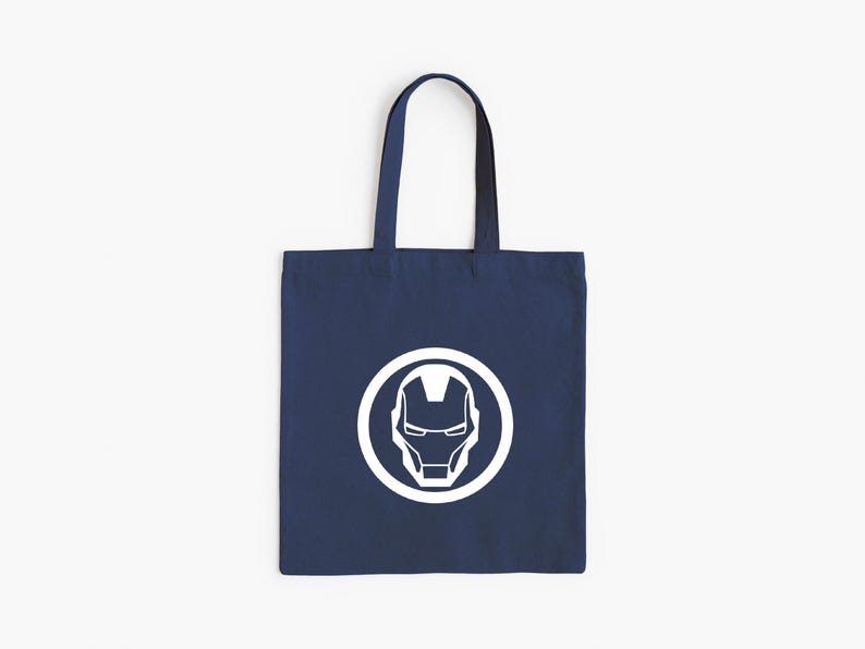 May include: Navy blue tote bag featuring a white Iron Man helmet logo inside a white circle. The bag has a rectangular shape with a handle for carrying. The design is simple and bold, suitable for everyday use.
