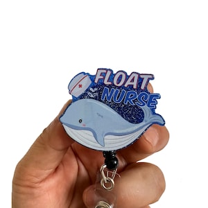 Könnte beinhalten: Blauer Glitzer-Badgehalter mit einem Cartoon-Wal, der eine Krankenschwestermütze trägt und den Text "FLOAT NURSE".