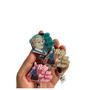 Könnte beinhalten: Drei verschiedene Ausweisrollen-Designs mit einer Frau in einem blauen Kleid und dem Text "Help is on the way dear" in rosa, gold und türkisfarbenem Glitzer.