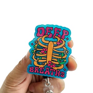 May include: A blue and pink glitter badge holder with a ribcage design and the text "DEEP BREATHS".