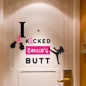 May include: A white door with a decorative sticker that reads "I KICKED Cancer's BUTT". The sticker features a pink ribbon, boxing gloves, and a silhouette of a person kicking. The door has a gold handle and is set in a wooden frame.
