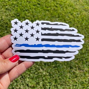 May include: A distressed American flag sticker with a thin blue line across the middle. The sticker is white with black stripes and blue stars.