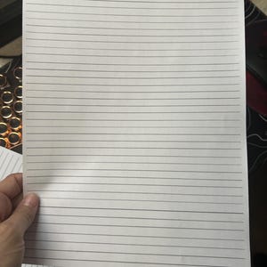 May include: A rectangular sheet of white paper featuring a series of evenly spaced, thin horizontal black lines printed across the entire surface. The paper is oriented vertically, providing a clean and uniform template for writing or note-taking.