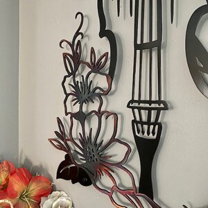 May include: Black metal wall art featuring a stylized violin with floral accents. The violin is outlined in black and the flowers are a gradient of brown and red.
