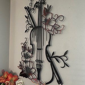 May include: Black metal wall art featuring a violin with floral accents. The violin is outlined in black and the flowers are in a copper color.