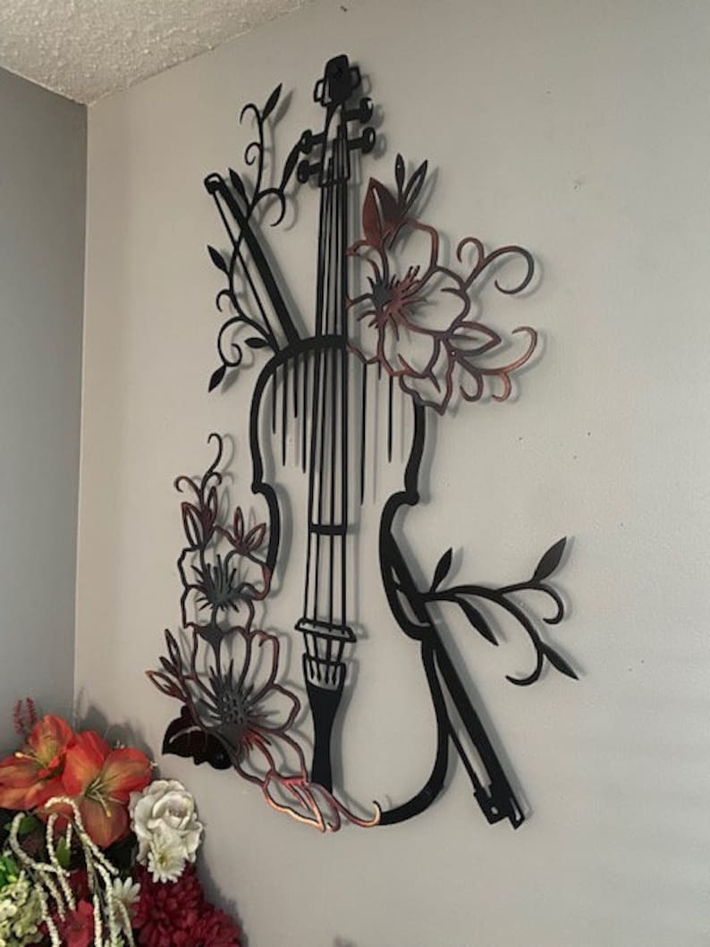 May include: Black metal wall art featuring a violin with floral accents. The violin is outlined in black and the flowers are in a copper color.