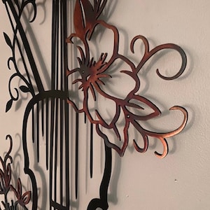 May include: A metal wall art sculpture of a violin with floral accents. The violin is black and the flowers are a copper color.