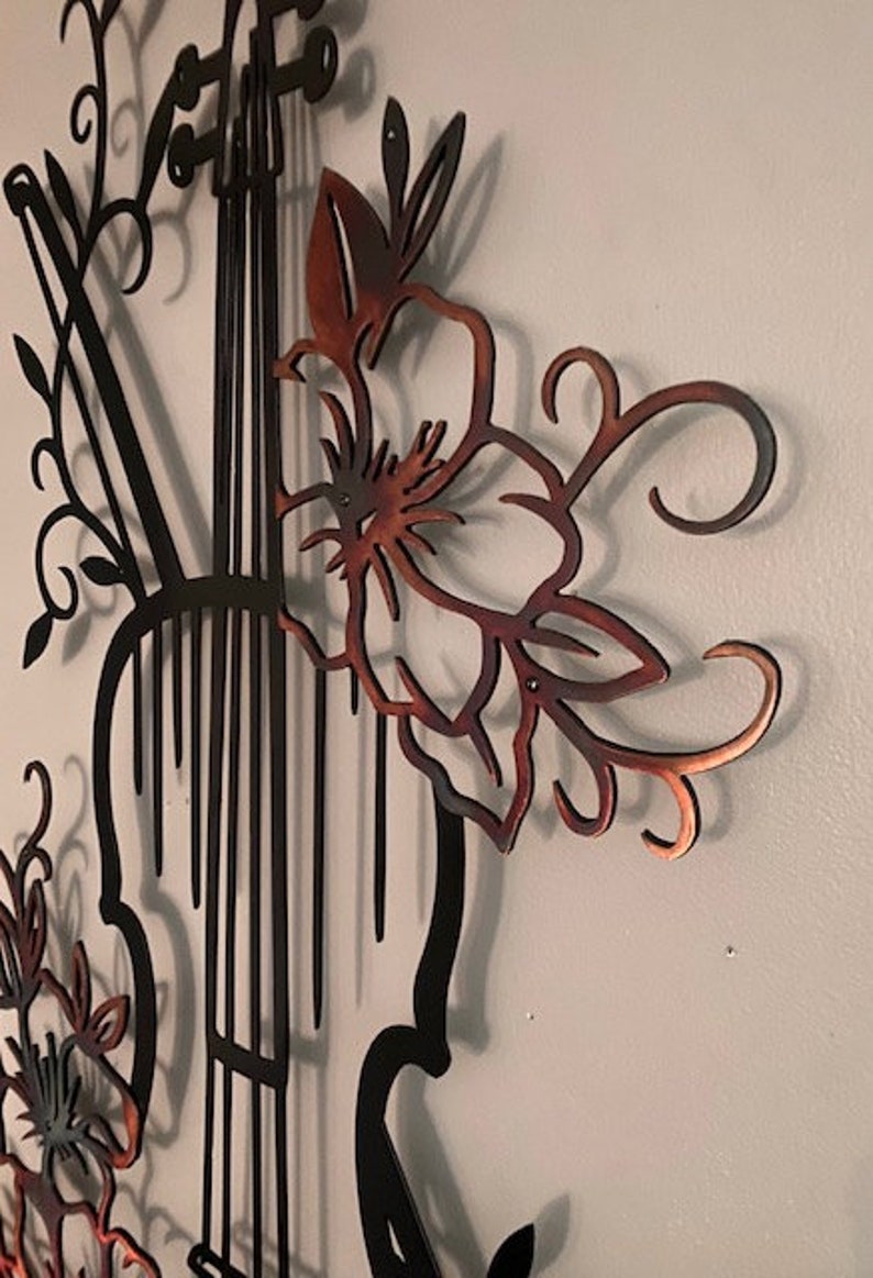 May include: A metal wall art sculpture of a violin with floral accents. The violin is black and the flowers are a copper color.