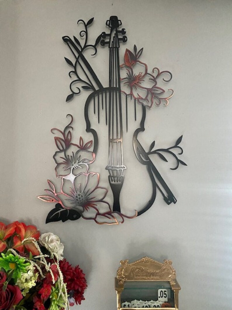 May include: Black metal wall art featuring a violin with floral accents. The violin is outlined in black and the flowers are a copper color.