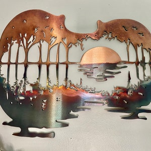 May include: A metal wall art sculpture of a sunset over a lake with trees in the foreground. The sculpture is shaped like a guitar and has a copper finish.