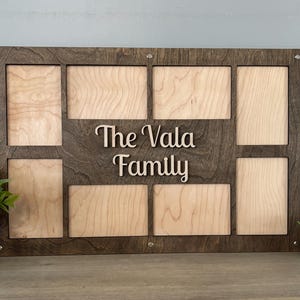 May include: A brown wooden picture frame with eight openings for photos. The frame has a light wood insert and the text "The Vala Family" is written in a decorative font.